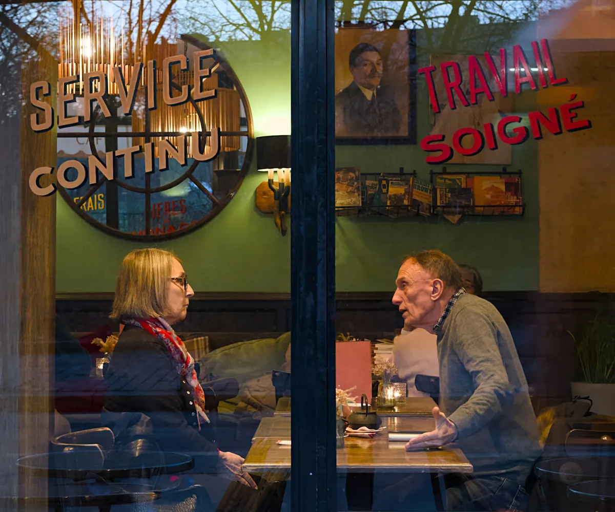 Two people in conversation, seen through the window of a Paris café.