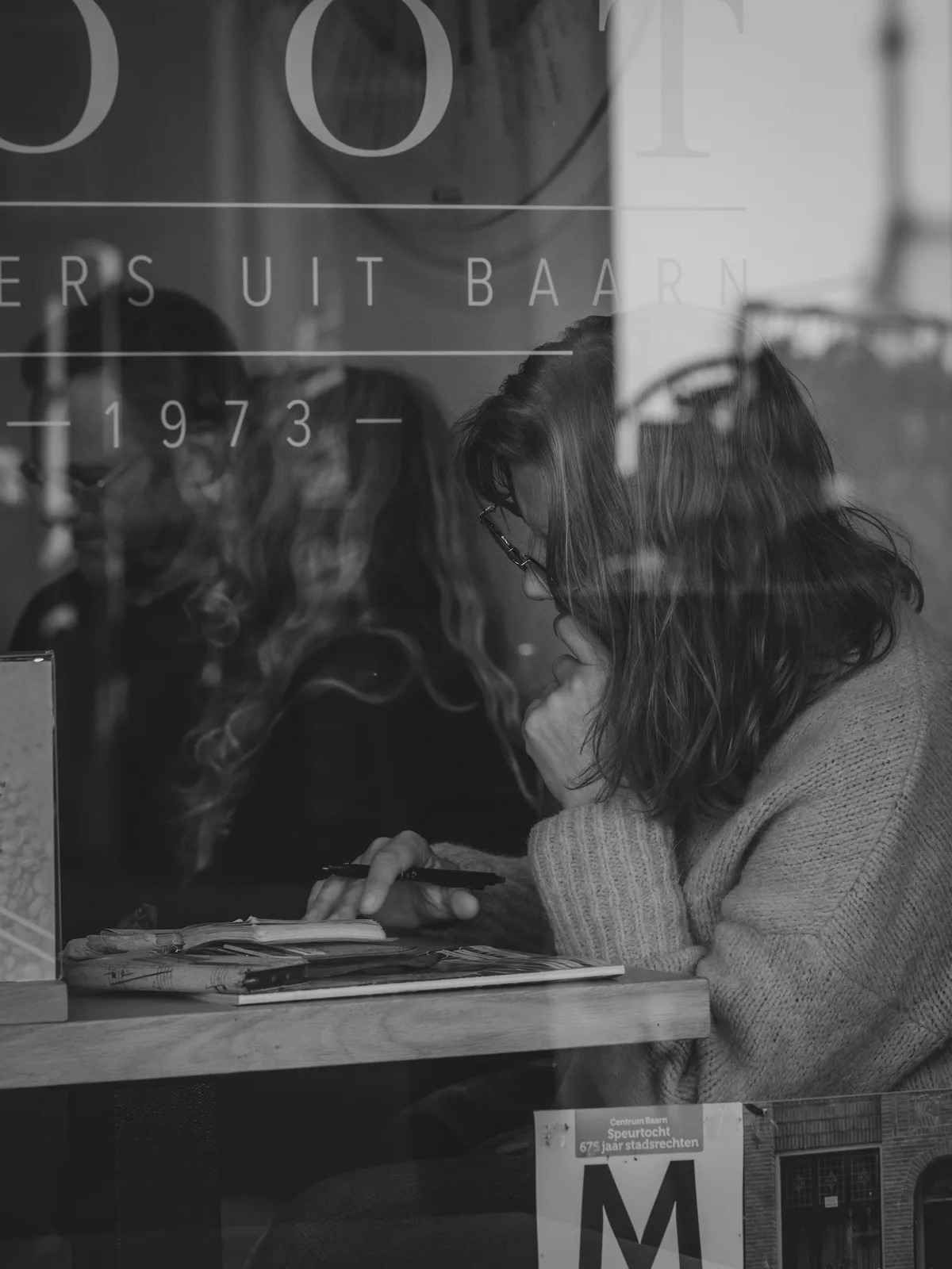 A person reading and taking notes inside a café, seen through the window.